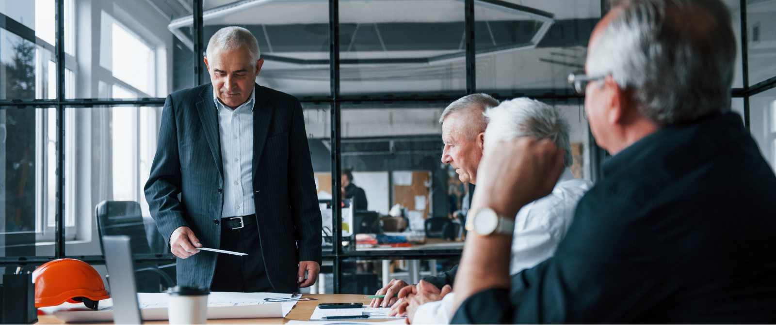Senior business leaders review documents and align on growth strategies; a construction helmet signals focus on sustainable scaling.