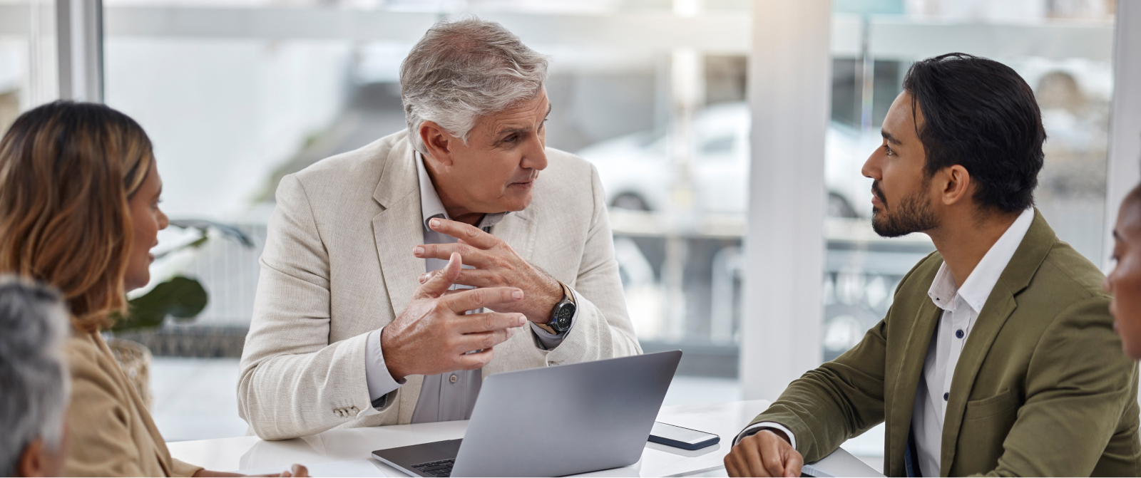 Three executives discuss scaling and alignment at a table, focusing on leadership and sustainable growth with a laptop open.