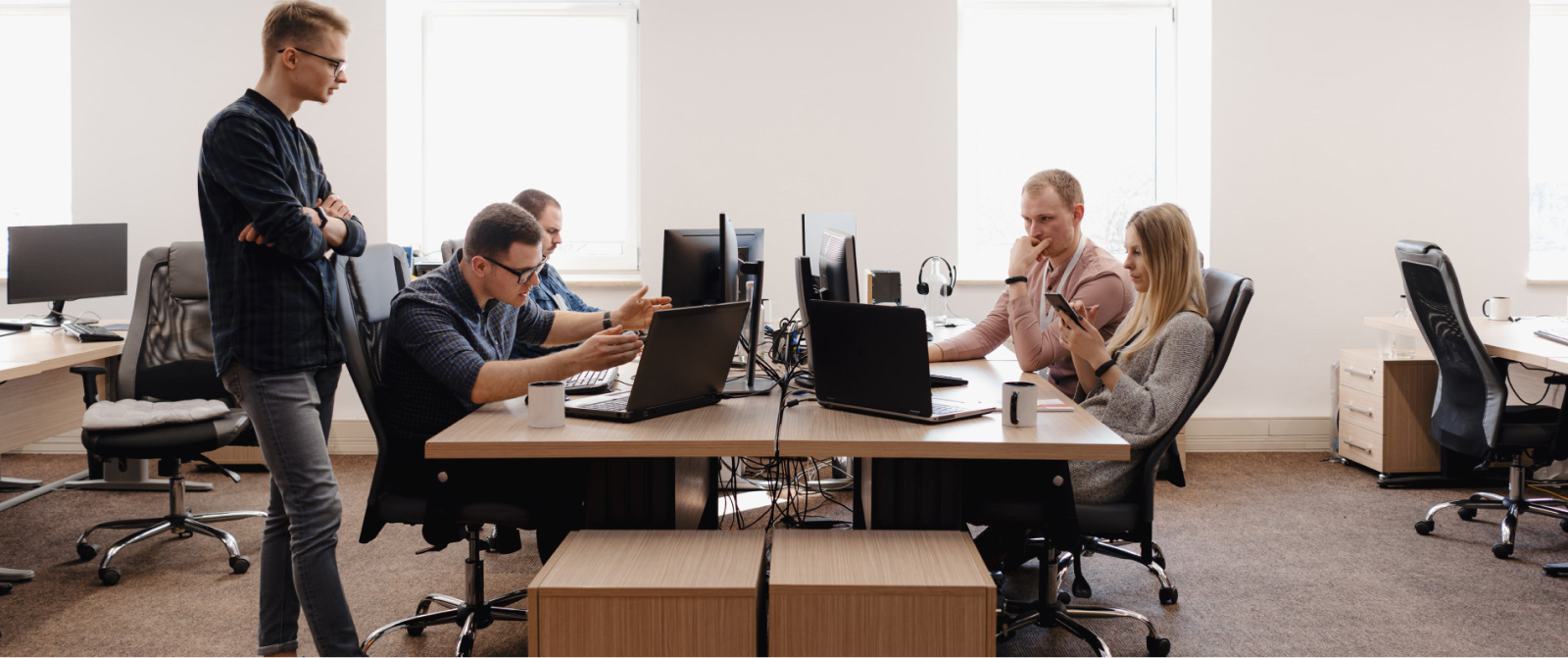 In a bright, modern office, a team discusses clarity and alignment as a leader observes, fostering systems thinking for growth.