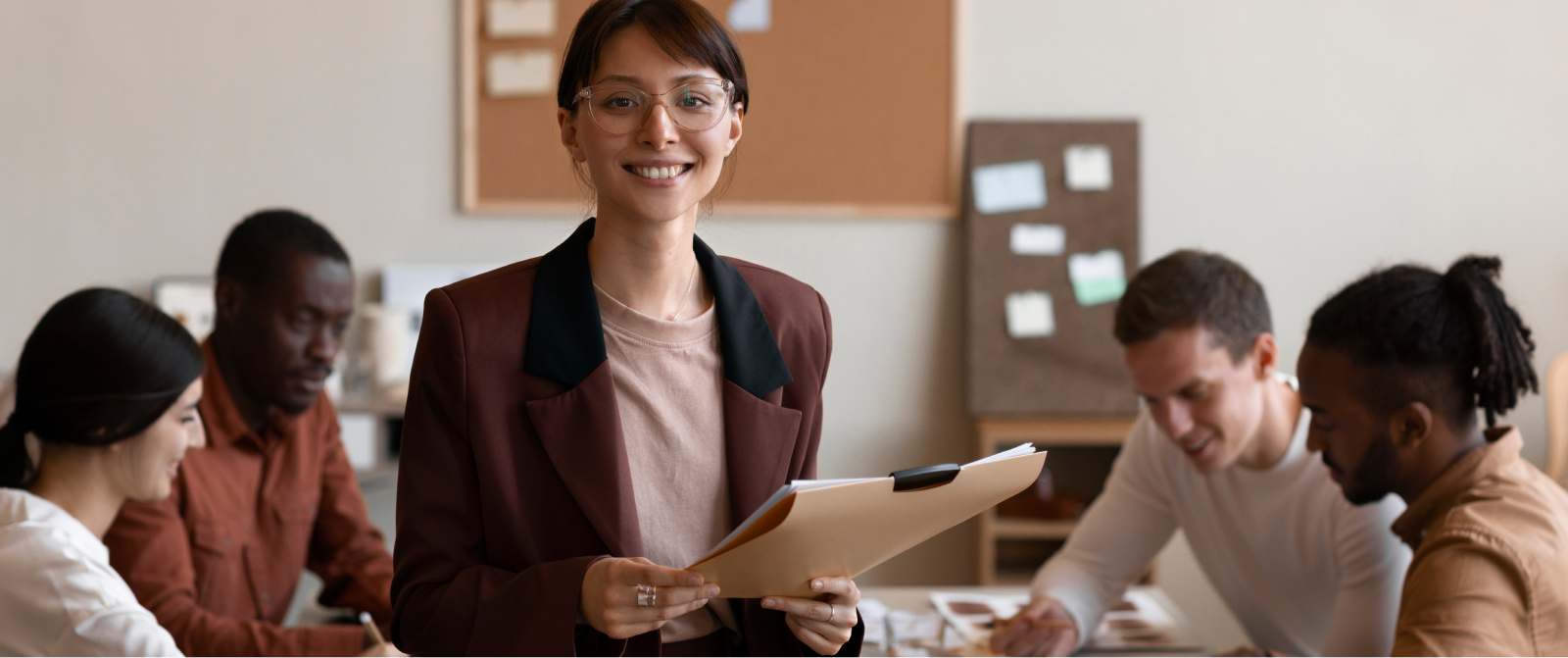 Smiling woman in a blazer holds a folder as her team collaborates on scaling, clarity, and leadership for sustainable growth.