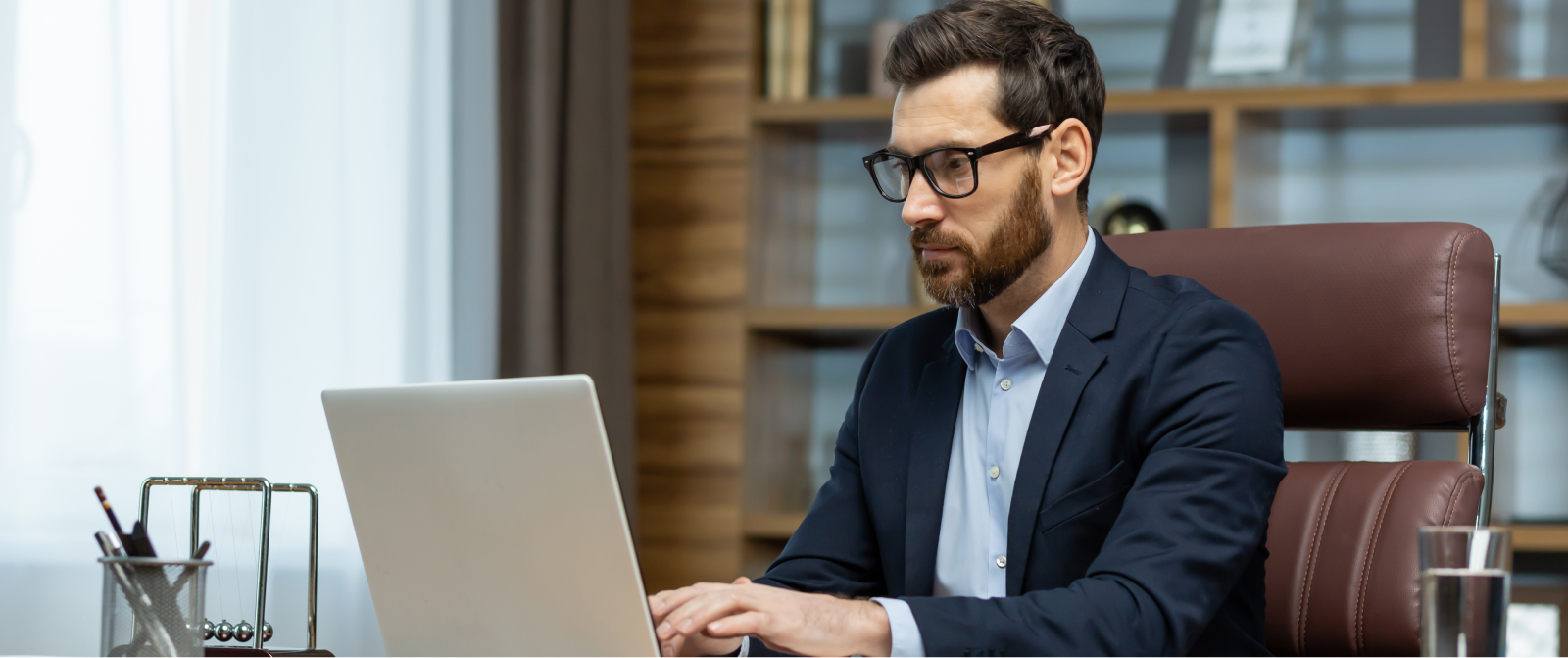 An executive in glasses and a dark suit works on a laptop, focusing on systems that drive alignment and sustainable growth.