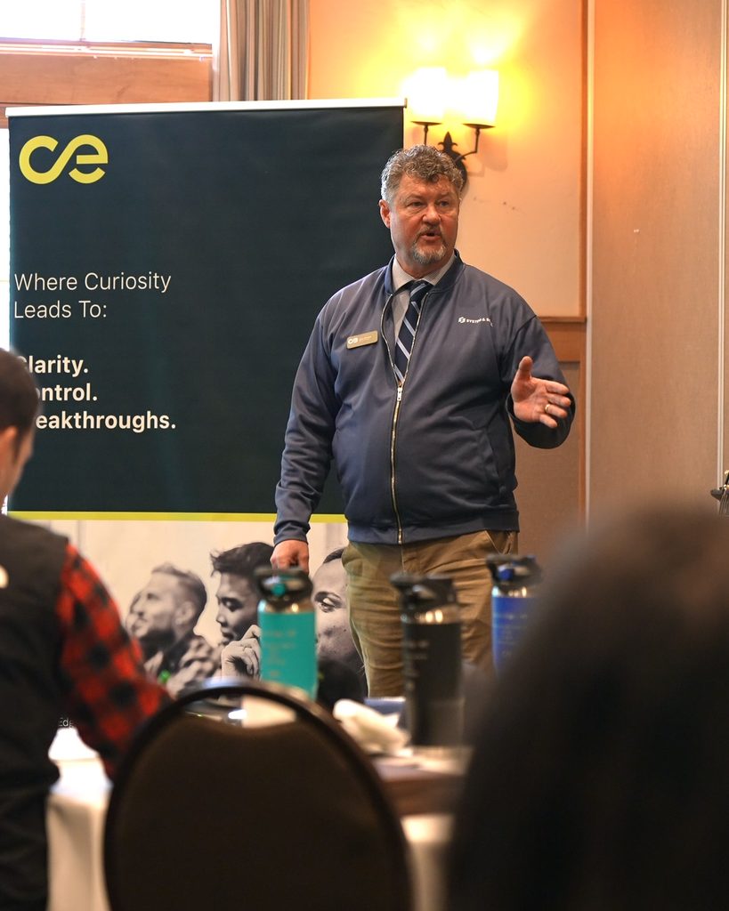 A speaker leads a workshop on leadership and sustainable growth, framed by a sign focused on clarity and breakthroughs.