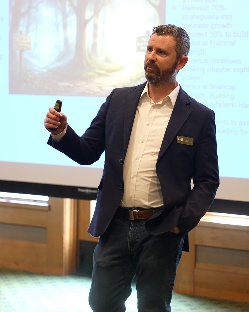 A leader in a blazer presenting sustainable growth strategies and systems thinking before a projection screen.