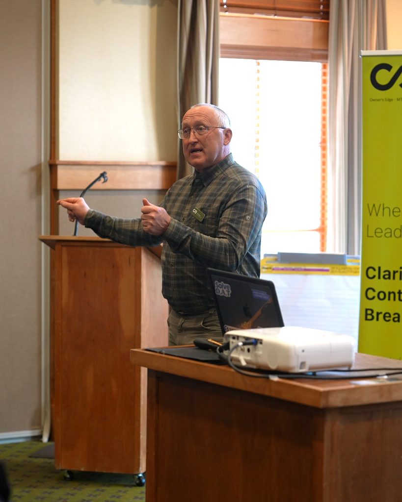 A leader in a plaid shirt presenting strategies for sustainable growth and organizational alignment at a podium.