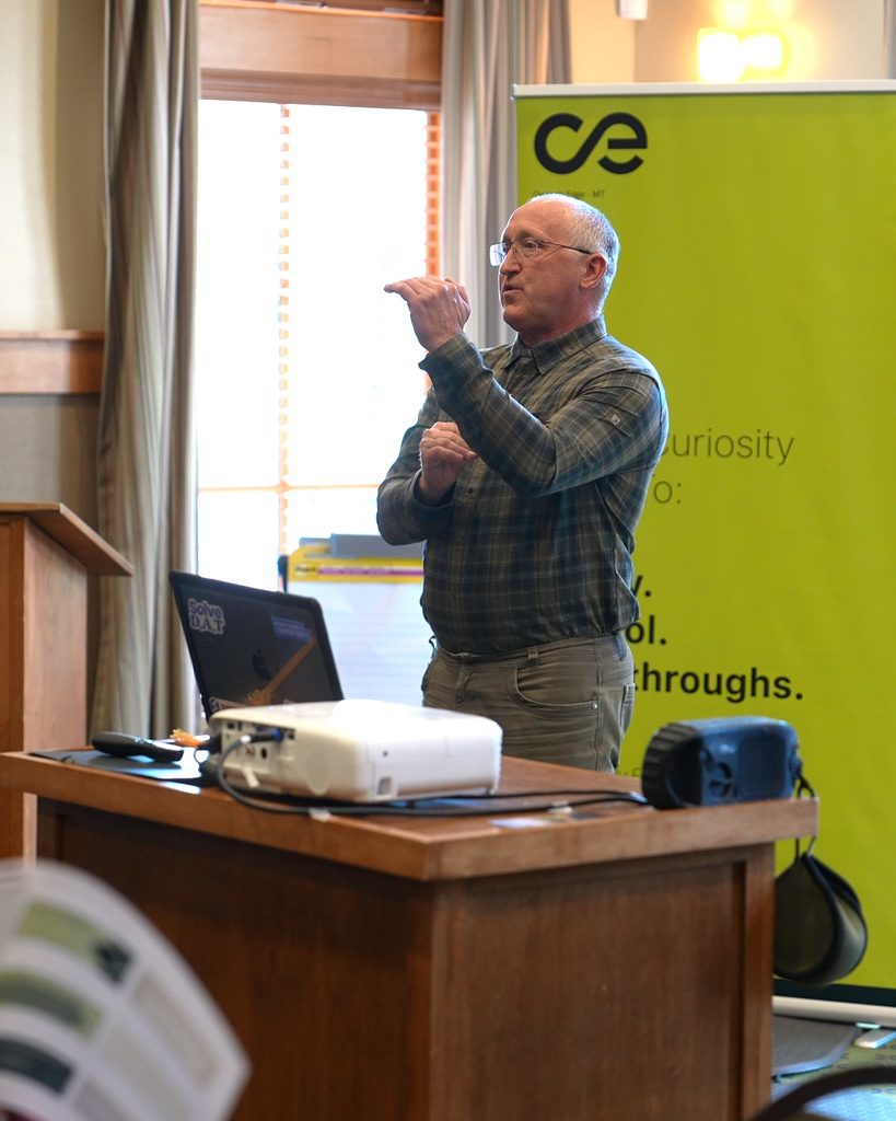 A speaker leads a session on sustainable growth and systems thinking at a podium.