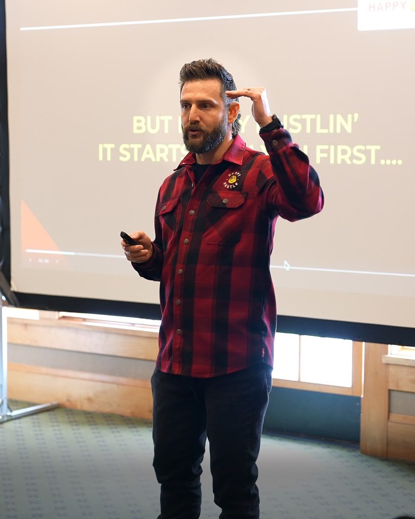 A speaker in a plaid shirt presents on leadership and sustainable growth to an audience.