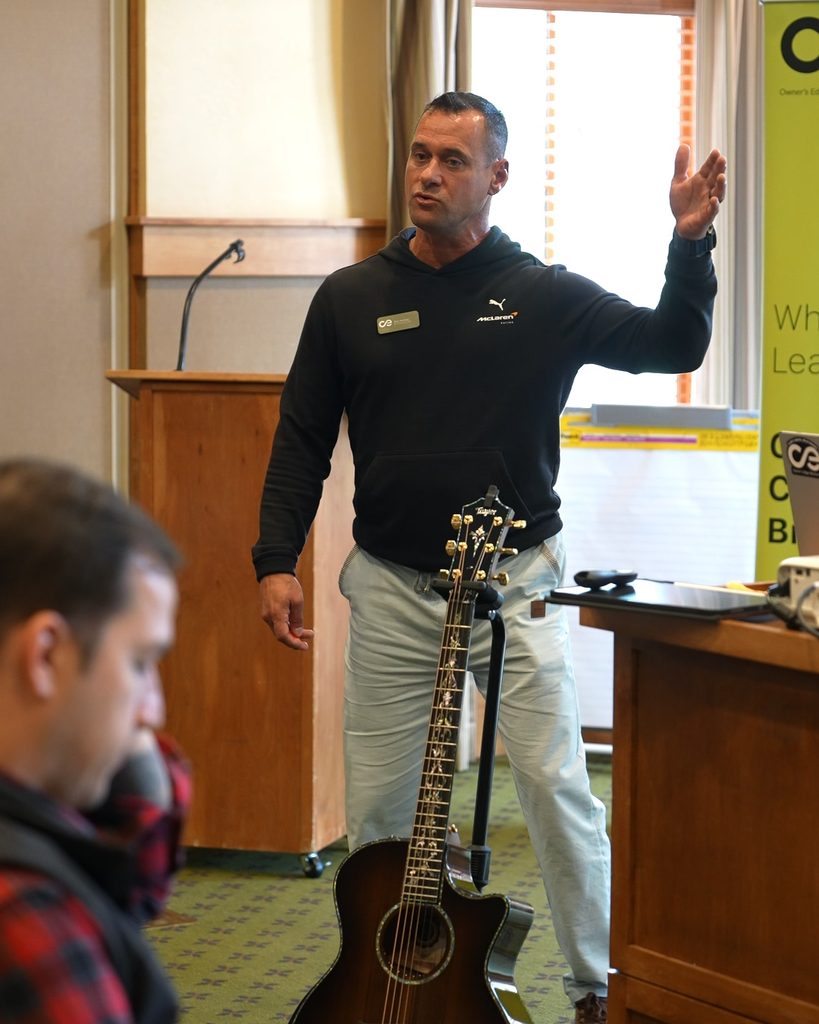 A leader speaks to an audience in a conference room, using systems thinking to inspire alignment and sustainable growth.