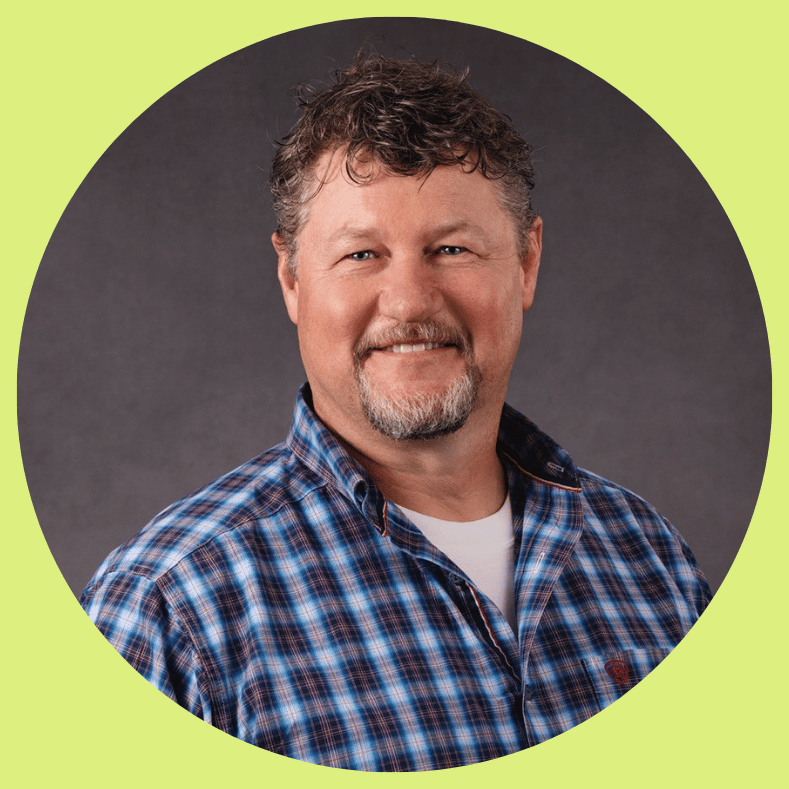 Professional headshot of a smiling leader with a goatee, wearing a blue plaid button-down shirt.